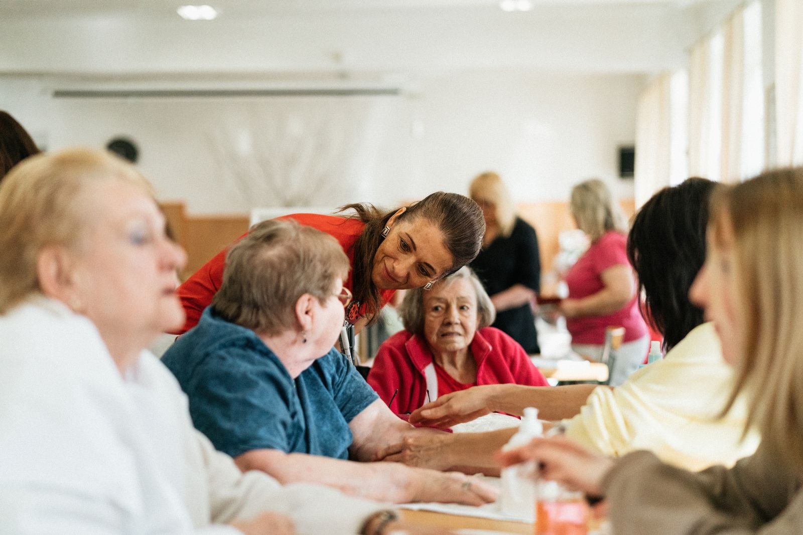 A caregiver assisting a group of older adults together at a table in a senior community setting